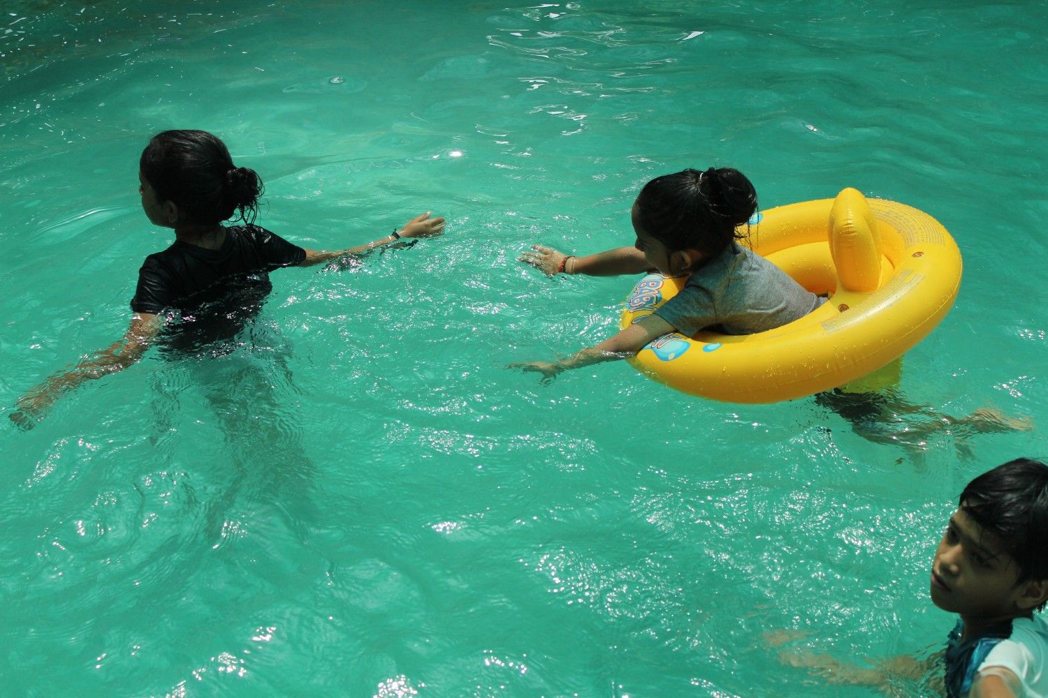 Children enjoying a swim in a pool, including a girl floating in a yellow inflatable ring