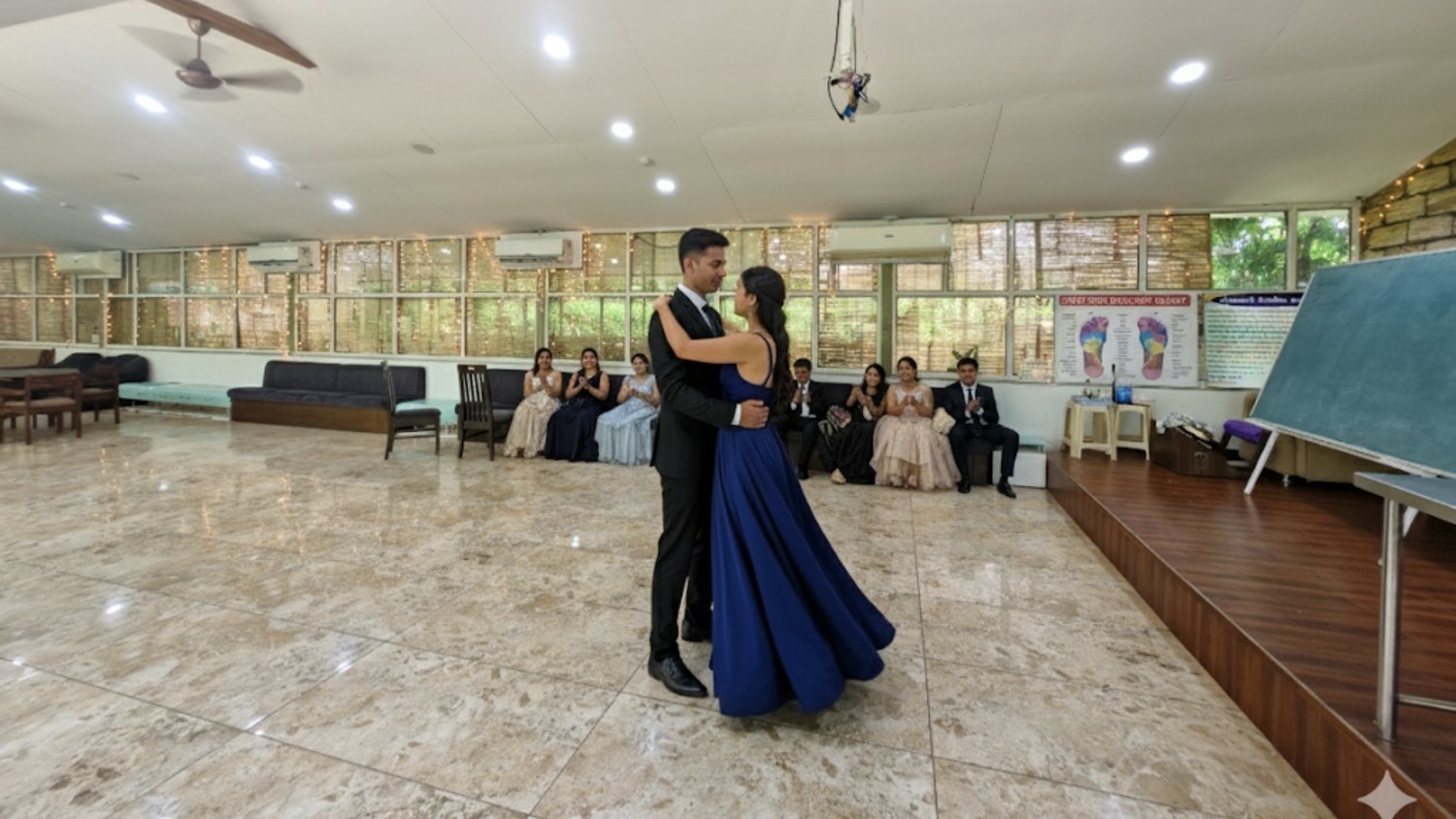 Couple dancing in a spacious indoor hall while guests seated in the background watch the performance.