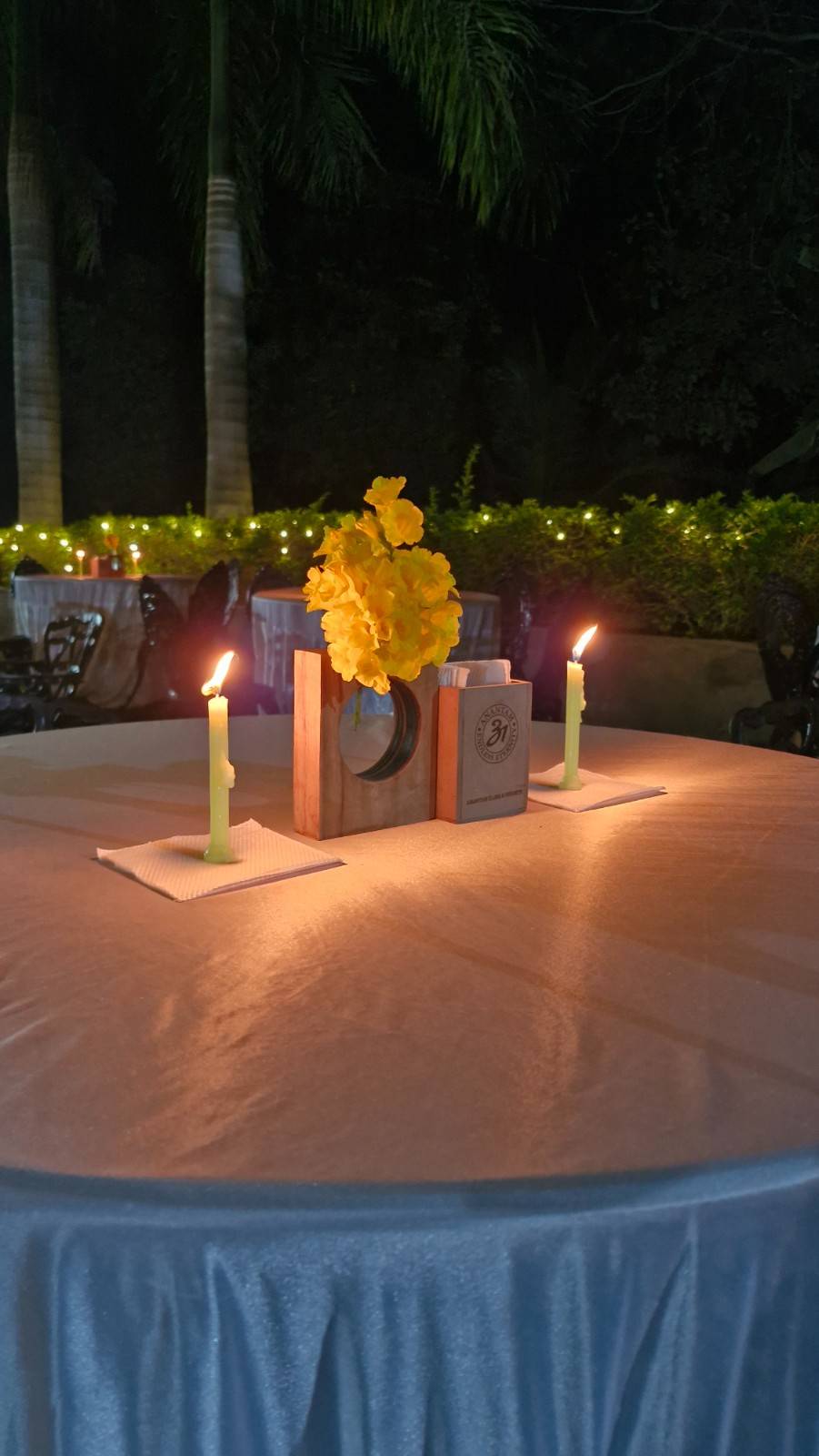 Close-up of an outdoor dining table with a yellow floral centerpiece and two lit candles